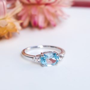 Bague pour femme en argent rhodié sertie d'une topaze bleue ovale et de petites topazes incolores autour